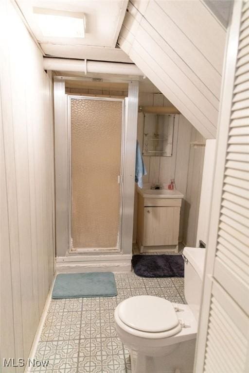 bathroom featuring wood walls, sink, a shower with shower door, and toilet