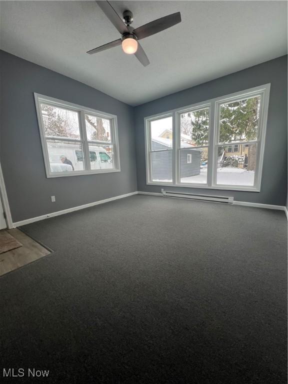 spare room featuring dark colored carpet, ceiling fan, and a baseboard heating unit