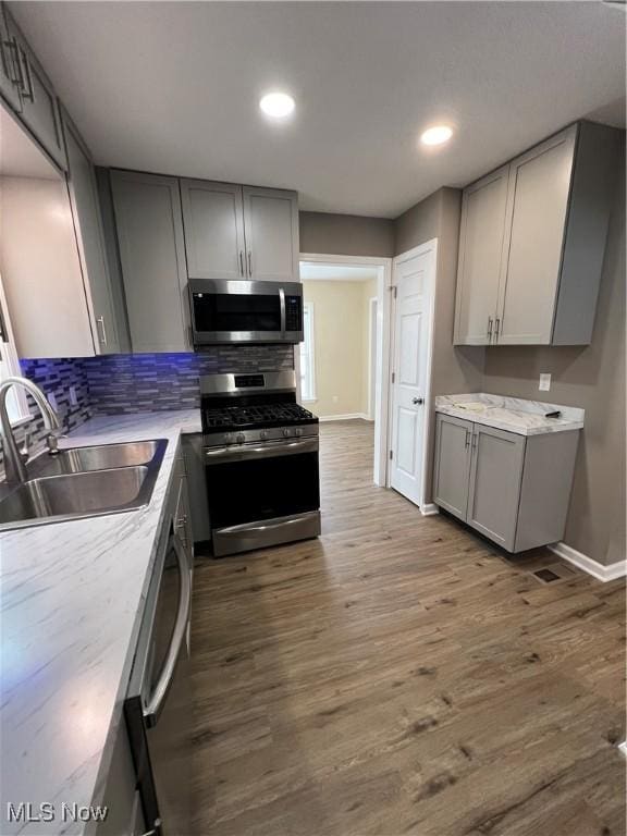 kitchen with hardwood / wood-style floors, appliances with stainless steel finishes, gray cabinetry, and sink