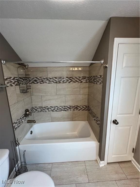 bathroom with tile patterned floors, a textured ceiling, toilet, and tiled shower / bath