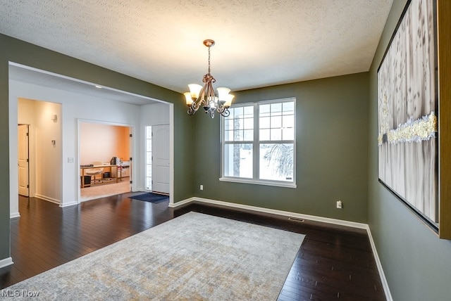 empty room featuring a notable chandelier, dark hardwood / wood-style floors, and a textured ceiling