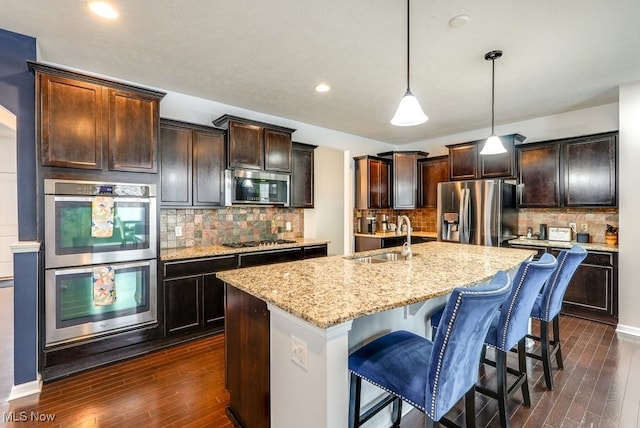 kitchen with decorative backsplash, stainless steel appliances, sink, pendant lighting, and a center island with sink