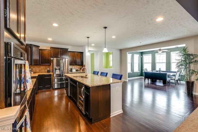 kitchen featuring hanging light fixtures, backsplash, an island with sink, a textured ceiling, and appliances with stainless steel finishes