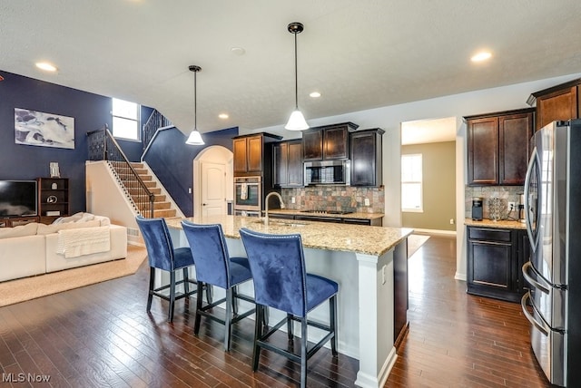 kitchen with tasteful backsplash, stainless steel appliances, a kitchen island with sink, sink, and pendant lighting