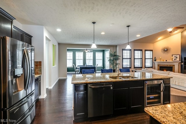 kitchen with wine cooler, light stone counters, decorative light fixtures, a textured ceiling, and appliances with stainless steel finishes