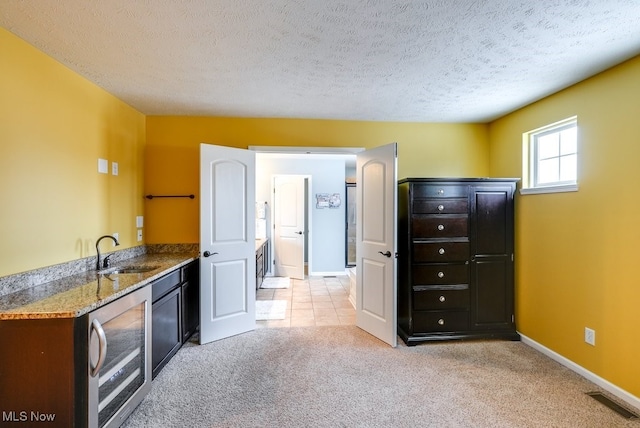 kitchen with light carpet, a textured ceiling, beverage cooler, sink, and stone countertops