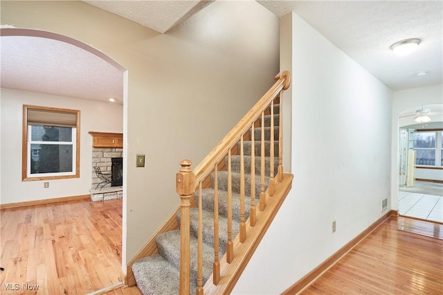 stairway with ceiling fan, a fireplace, wood-type flooring, and a textured ceiling