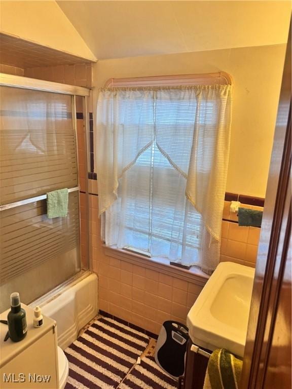 bathroom with combined bath / shower with glass door, vaulted ceiling, and tile walls