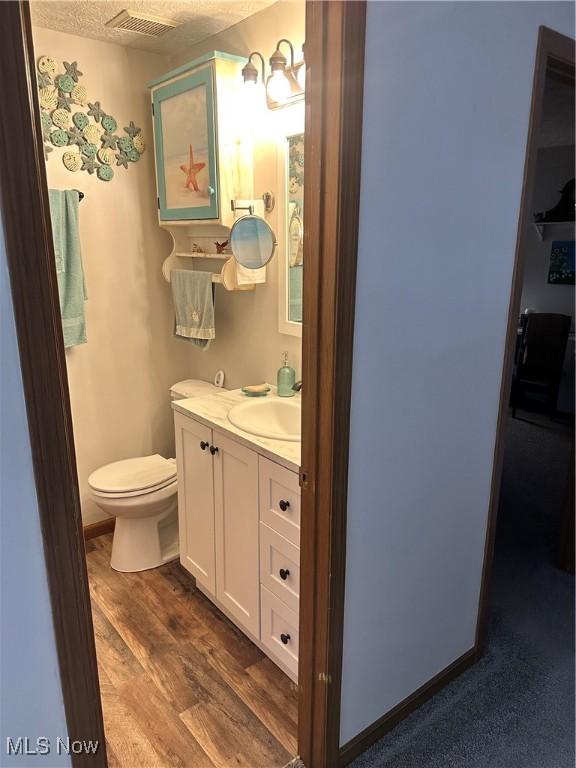 bathroom featuring wood-type flooring, vanity, a textured ceiling, and toilet