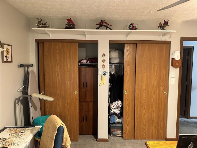 bedroom featuring ceiling fan, light colored carpet, multiple closets, and a textured ceiling