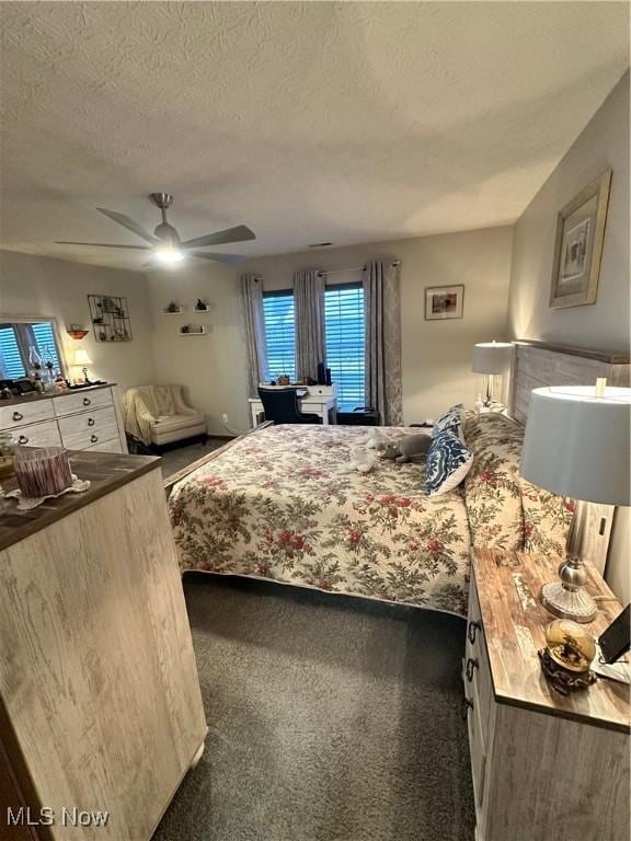 bedroom with ceiling fan, dark carpet, and a textured ceiling