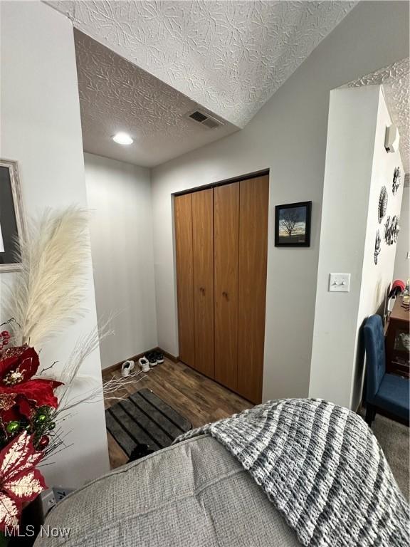 bedroom featuring dark hardwood / wood-style flooring, vaulted ceiling, a closet, and a textured ceiling