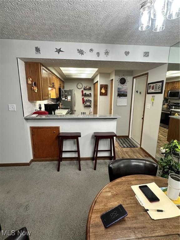 kitchen featuring light colored carpet, stainless steel appliances, kitchen peninsula, and a textured ceiling