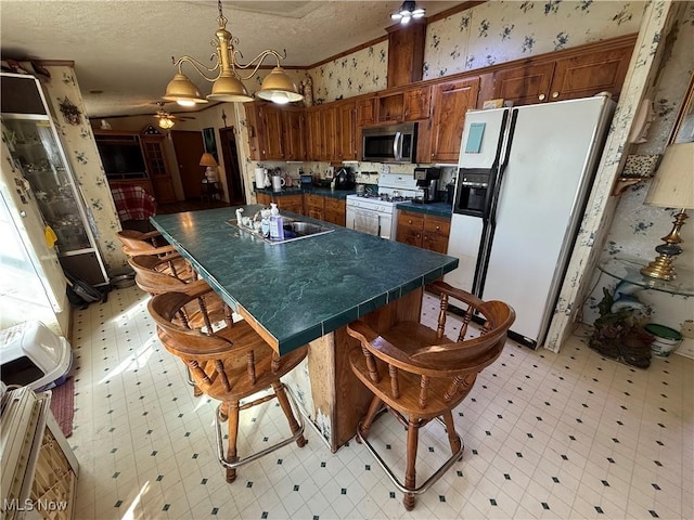 kitchen with dark countertops, wallpapered walls, light floors, white appliances, and a sink