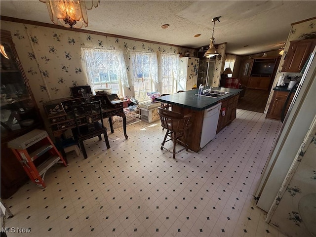 kitchen featuring wallpapered walls, white dishwasher, a sink, crown molding, and dark countertops