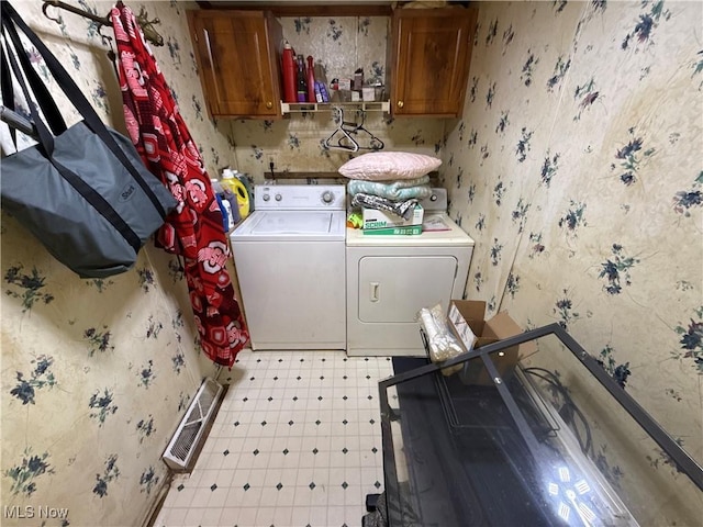 laundry room featuring washing machine and clothes dryer, cabinet space, wallpapered walls, and light floors