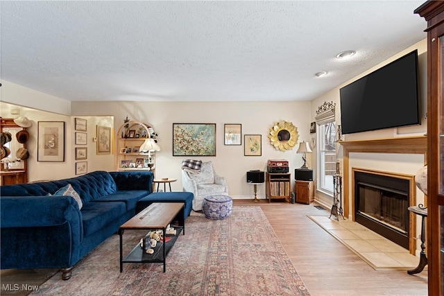 living room featuring a tile fireplace, light hardwood / wood-style floors, and a textured ceiling