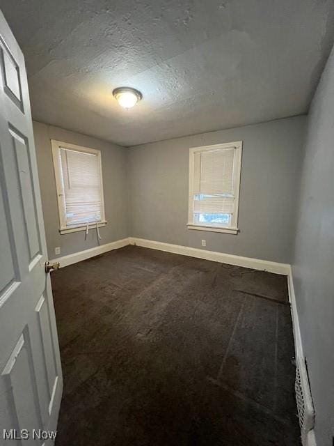 unfurnished room featuring a textured ceiling and dark carpet