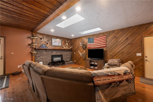 living room featuring beam ceiling, a wood stove, a skylight, wood walls, and wood-type flooring