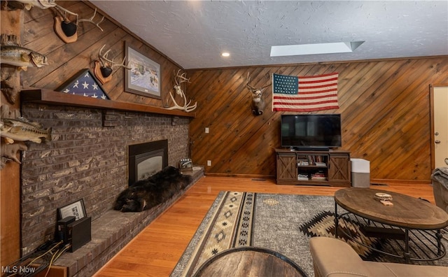 living room featuring a brick fireplace, a textured ceiling, hardwood / wood-style floors, and a skylight