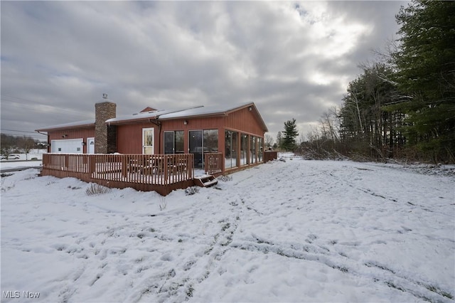 snow covered back of property featuring a garage and a deck