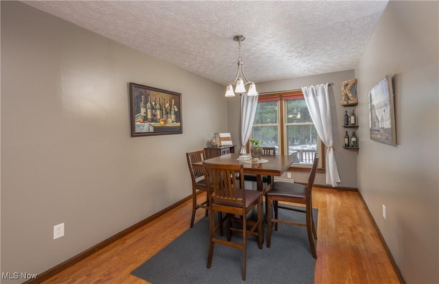 dining space with a textured ceiling, hardwood / wood-style flooring, and an inviting chandelier