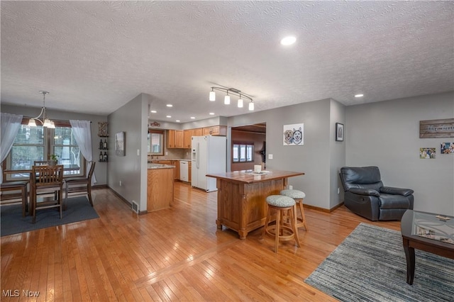 kitchen featuring pendant lighting, white appliances, a kitchen island, a textured ceiling, and light hardwood / wood-style floors