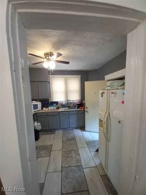 kitchen with gray cabinetry, ceiling fan, sink, a textured ceiling, and white appliances