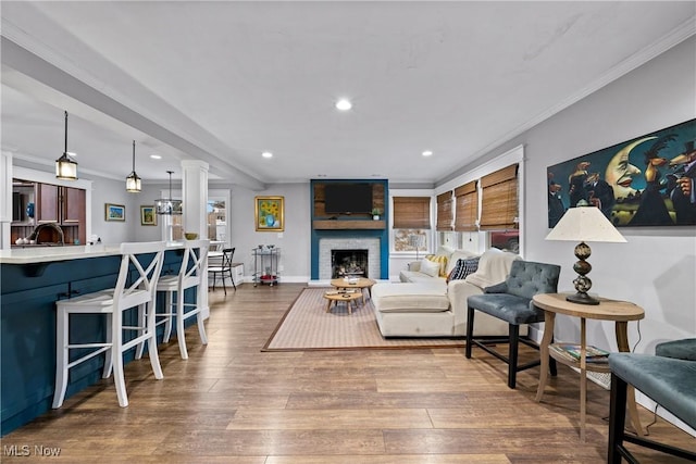 living room with sink, a brick fireplace, decorative columns, crown molding, and wood-type flooring