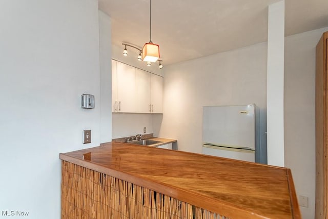 bar featuring white fridge, white cabinetry, hanging light fixtures, and sink