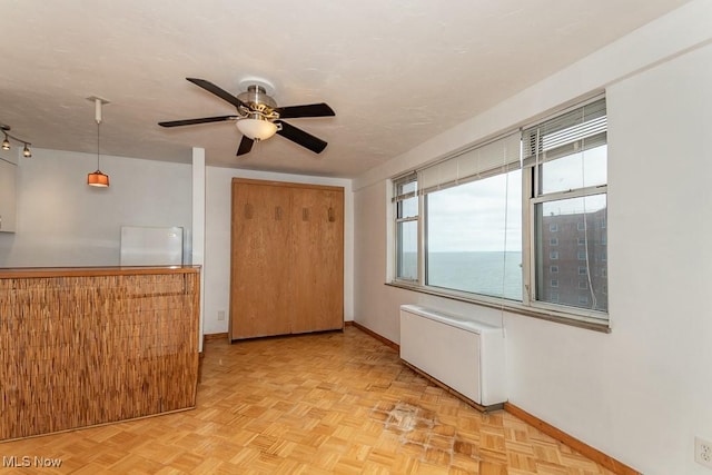 empty room featuring ceiling fan, a water view, radiator, and light parquet floors