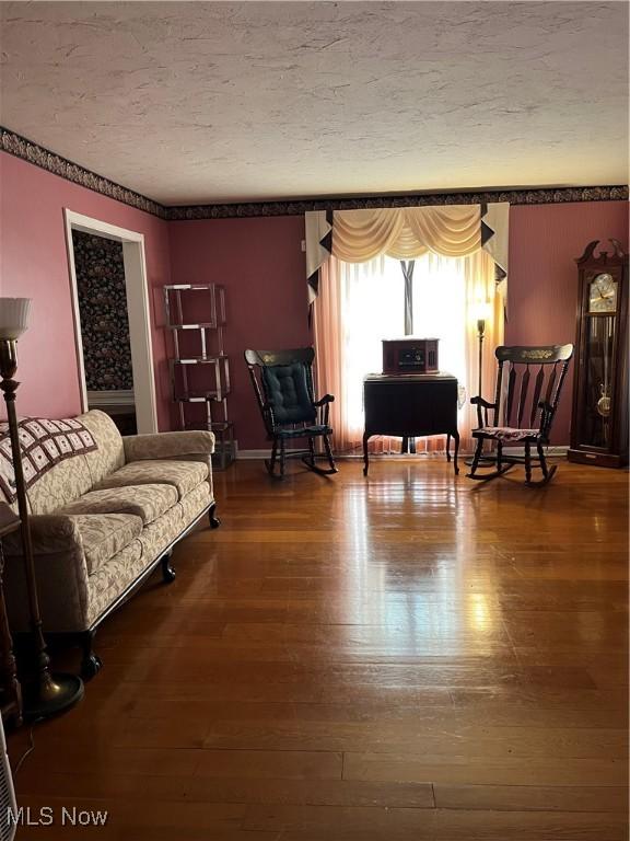 living room with a textured ceiling, baseboards, and wood finished floors