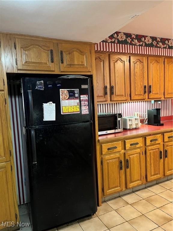 kitchen with light tile patterned floors, stainless steel microwave, brown cabinets, and freestanding refrigerator