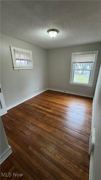 empty room featuring a textured ceiling, dark hardwood / wood-style floors, and a wealth of natural light