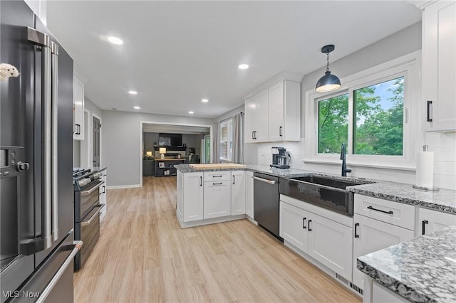 kitchen featuring white cabinetry, stainless steel appliances, kitchen peninsula, pendant lighting, and light wood-type flooring