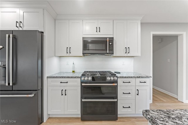 kitchen with backsplash, light wood-type flooring, light stone counters, white cabinetry, and stainless steel appliances