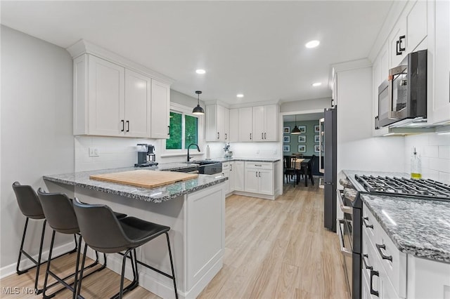 kitchen featuring kitchen peninsula, light stone counters, stainless steel range with gas cooktop, white cabinetry, and hanging light fixtures