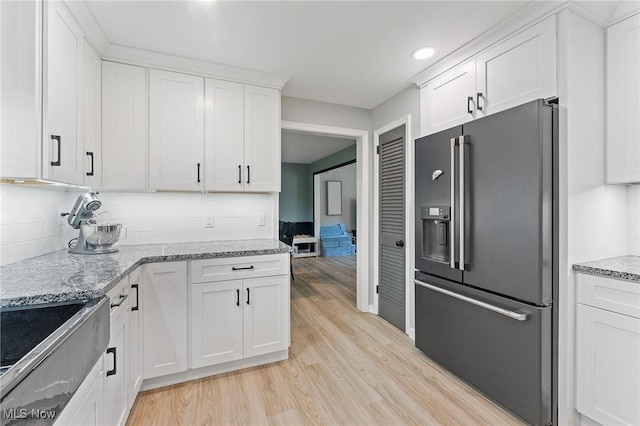 kitchen featuring white cabinetry, tasteful backsplash, light stone counters, light hardwood / wood-style flooring, and stainless steel fridge