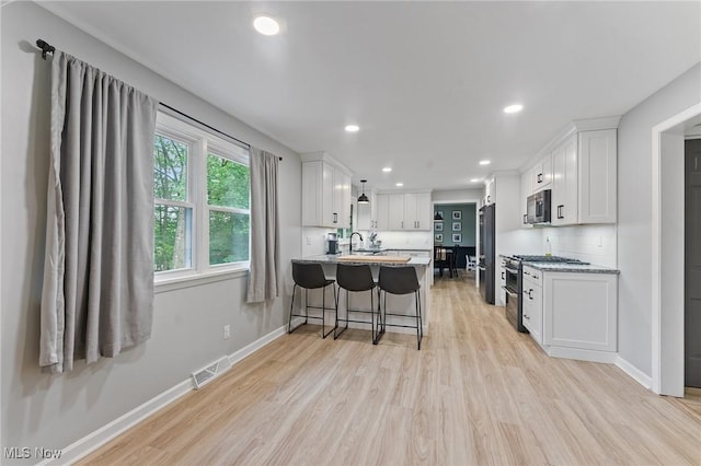 kitchen with white cabinets, a kitchen breakfast bar, light wood-type flooring, kitchen peninsula, and stainless steel appliances