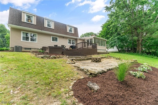 back of property featuring a wooden deck, cooling unit, an outdoor fire pit, a sunroom, and a lawn