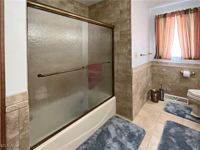 bathroom with tile patterned flooring, combined bath / shower with glass door, tile walls, and toilet