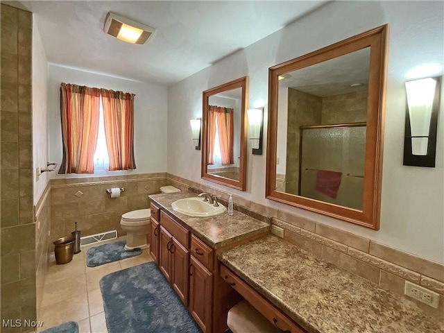 bathroom with walk in shower, tile patterned flooring, toilet, vanity, and tile walls