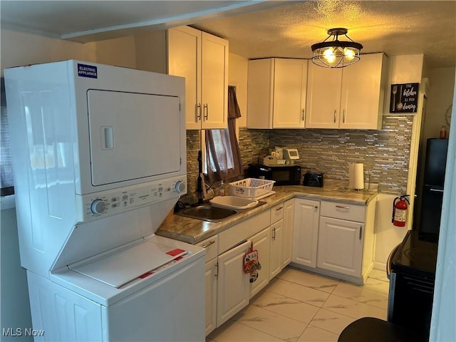 kitchen with black appliances, stacked washing maching and dryer, white cabinetry, and backsplash