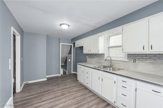 kitchen with tasteful backsplash, white cabinetry, hardwood / wood-style flooring, and sink