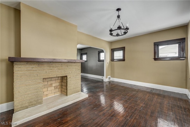 unfurnished living room featuring a chandelier, a fireplace, and dark wood-type flooring