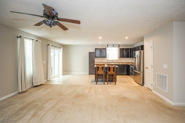 kitchen featuring a kitchen bar, appliances with stainless steel finishes, light carpet, a kitchen island, and plenty of natural light