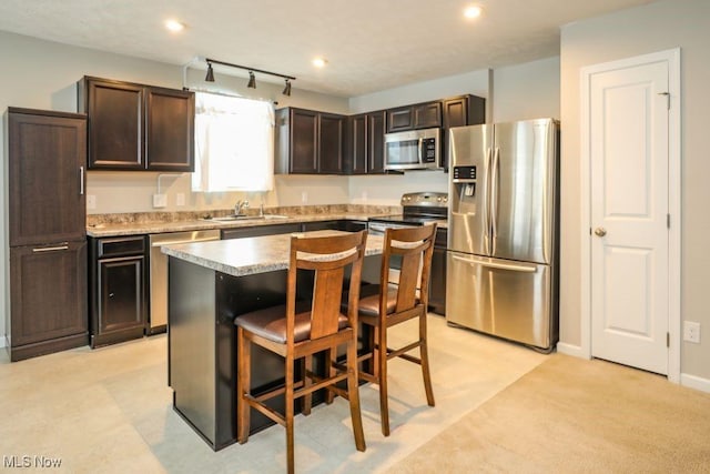 kitchen with dark brown cabinetry, a center island, sink, stainless steel appliances, and a breakfast bar