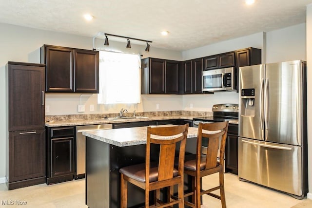 kitchen featuring appliances with stainless steel finishes, dark brown cabinets, sink, a center island, and a breakfast bar area