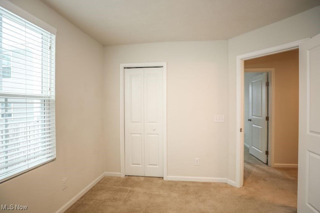 unfurnished bedroom with multiple windows, a closet, and light colored carpet