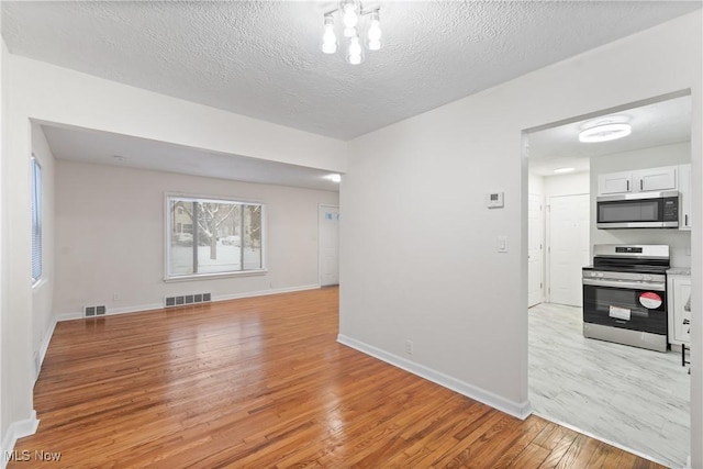 empty room featuring an inviting chandelier, a textured ceiling, and light hardwood / wood-style flooring